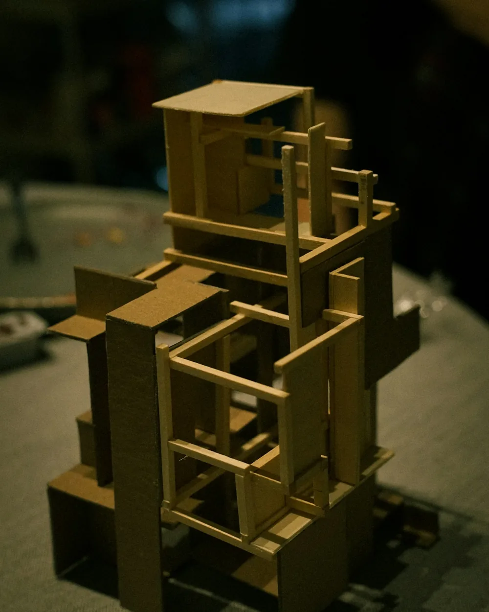 Maqueta de estructura de un edificio construida con cartón y listones finos de madera sobre una mesa de taller